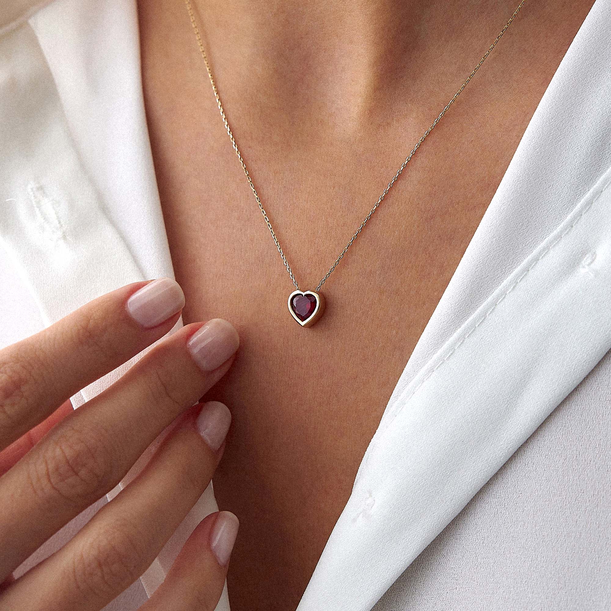 Necklace with a heart-shaped pendant worn by a person in a white outfit.