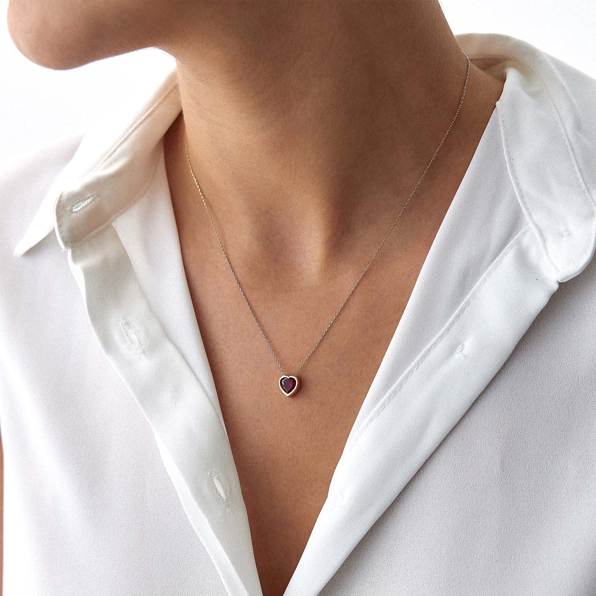 Necklace with a heart-shaped pendant worn by a person in a white shirt.