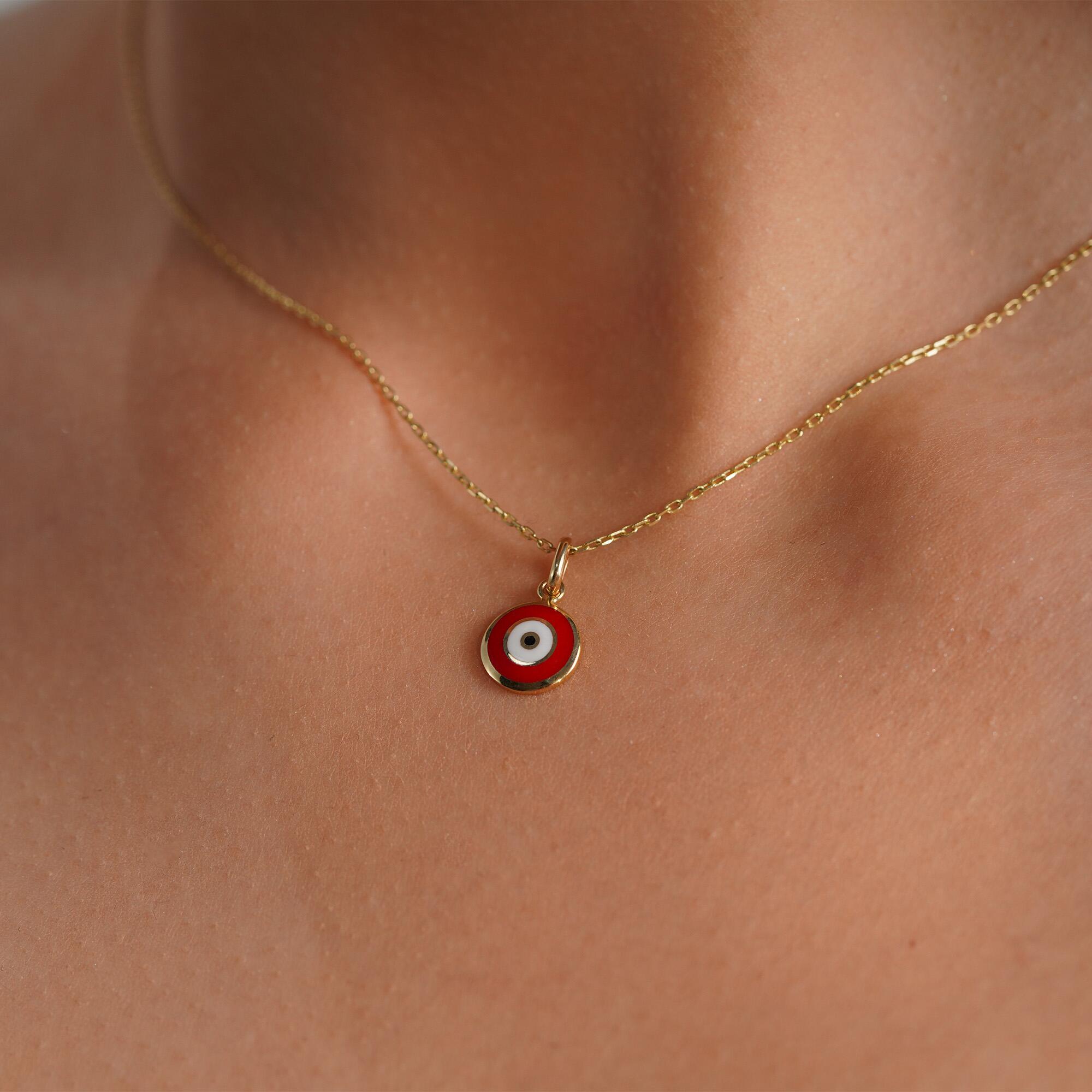 A red evil eye necklace in 14K yellow gold, displayed on a person's neck.