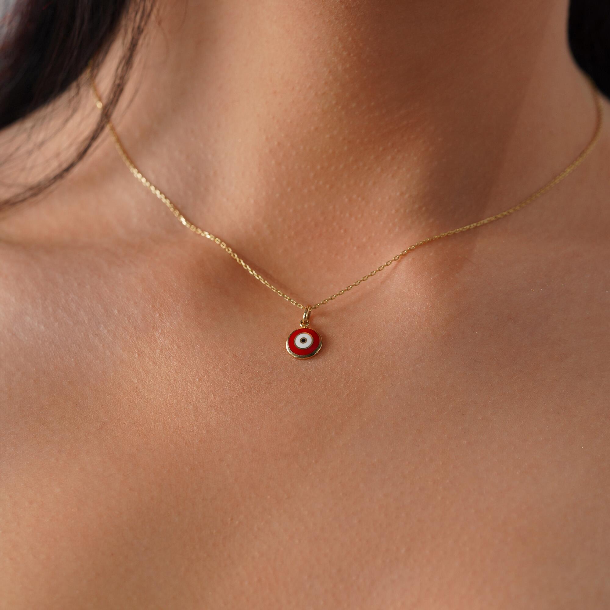 A red evil eye necklace in 14K yellow gold, displayed on a person's neck.