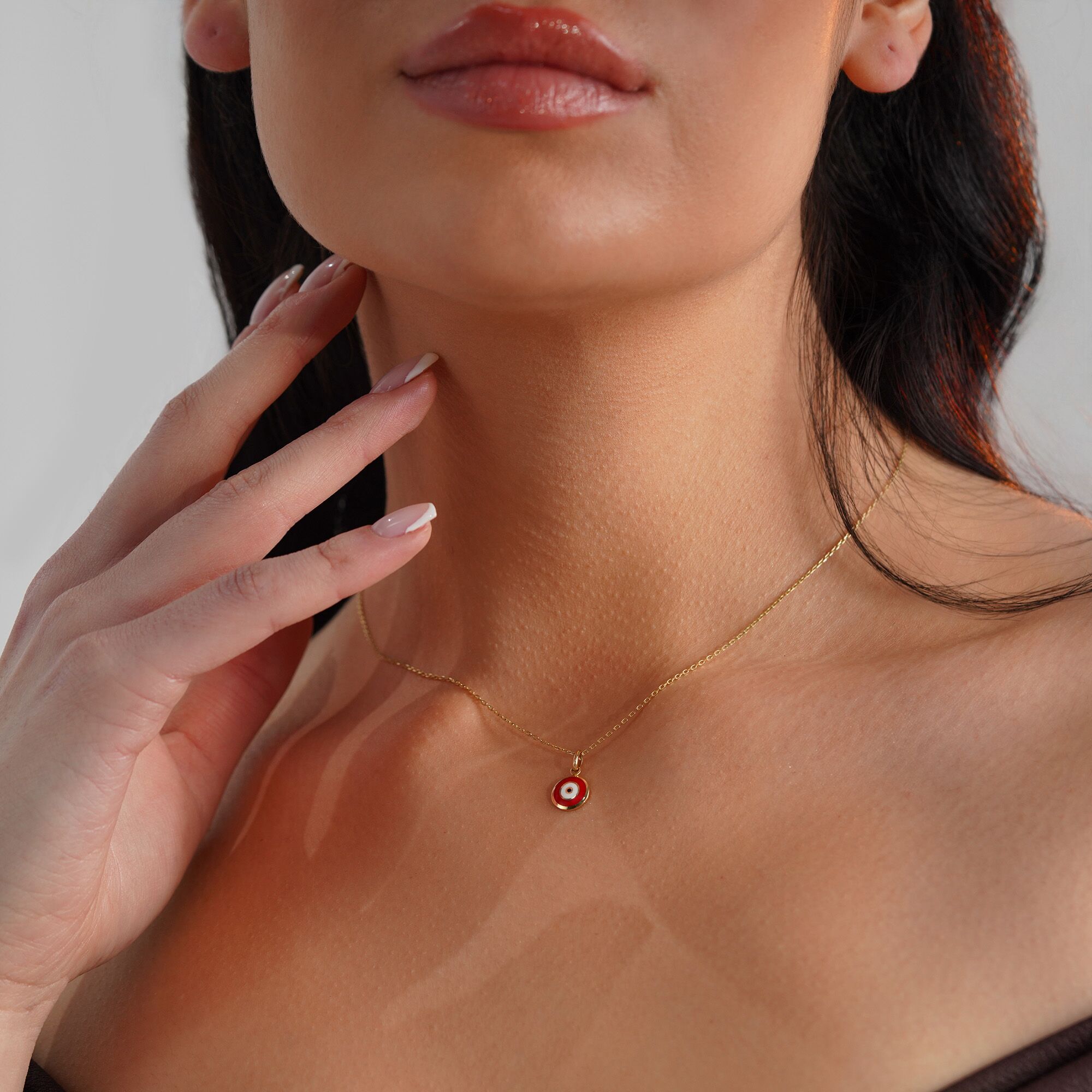 A red evil eye necklace in 14K yellow gold, displayed on a person's neck.