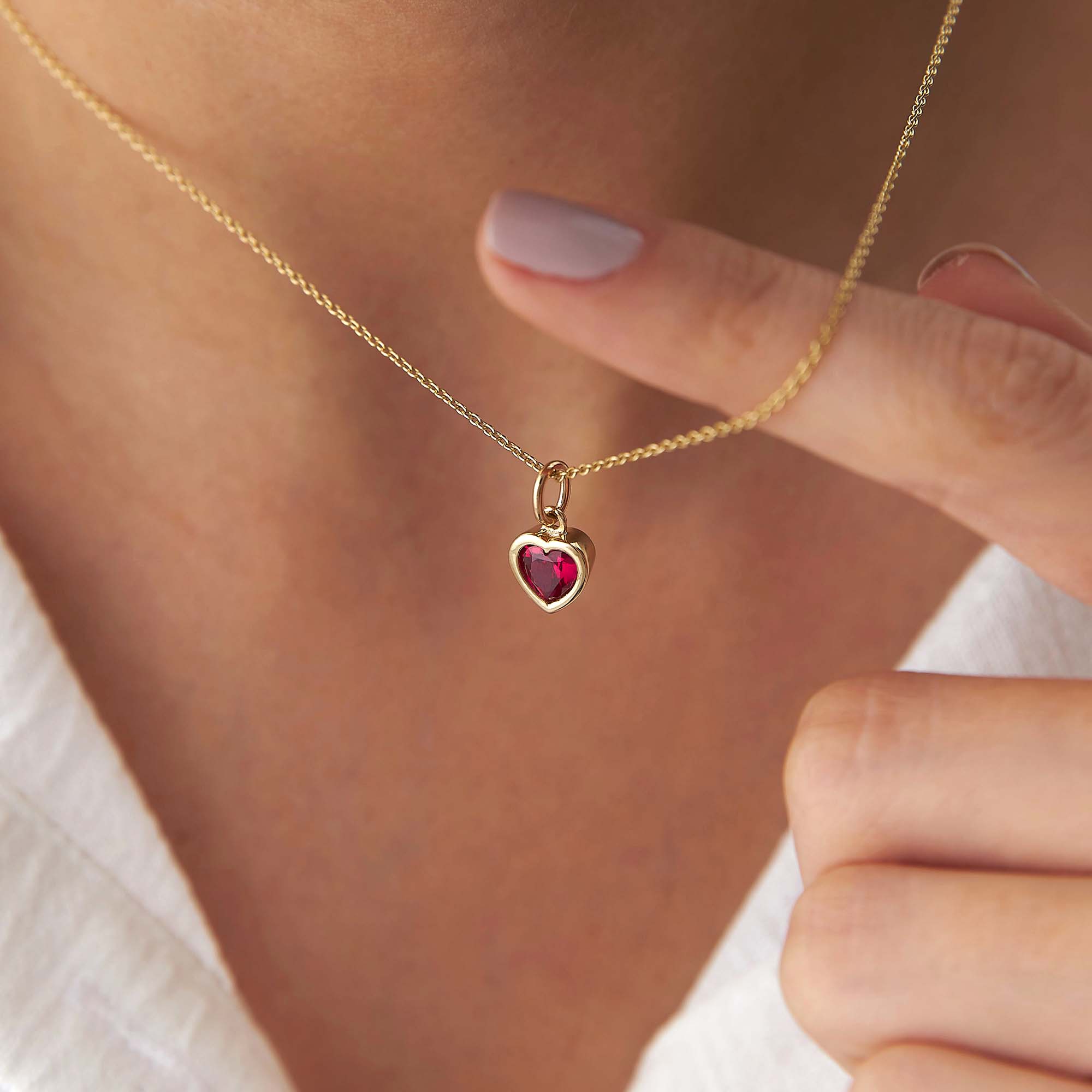 Gold necklace with a heart-shaped red gemstone pendant held by a hand.