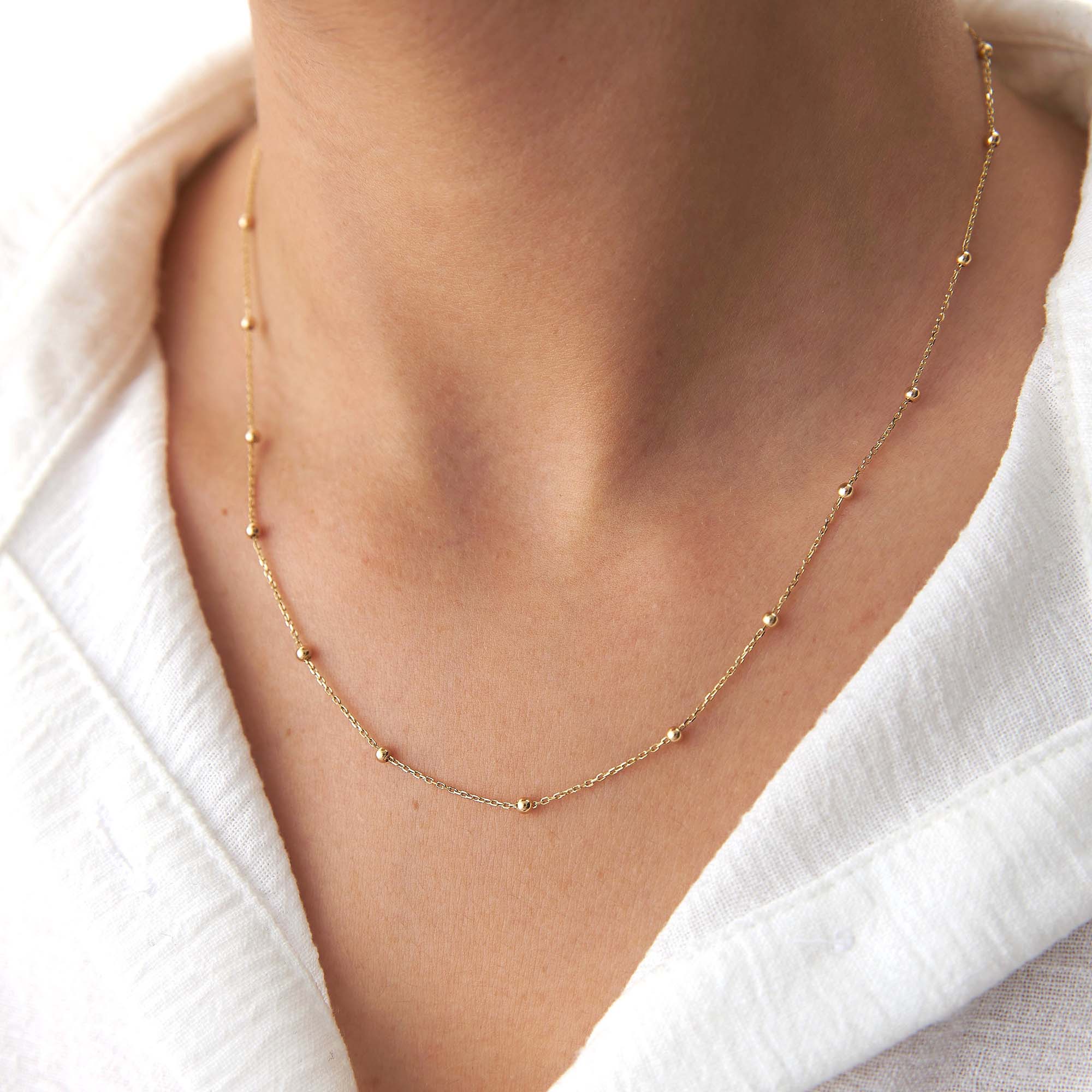 A 14k yellow gold satellite chain necklace on a model.