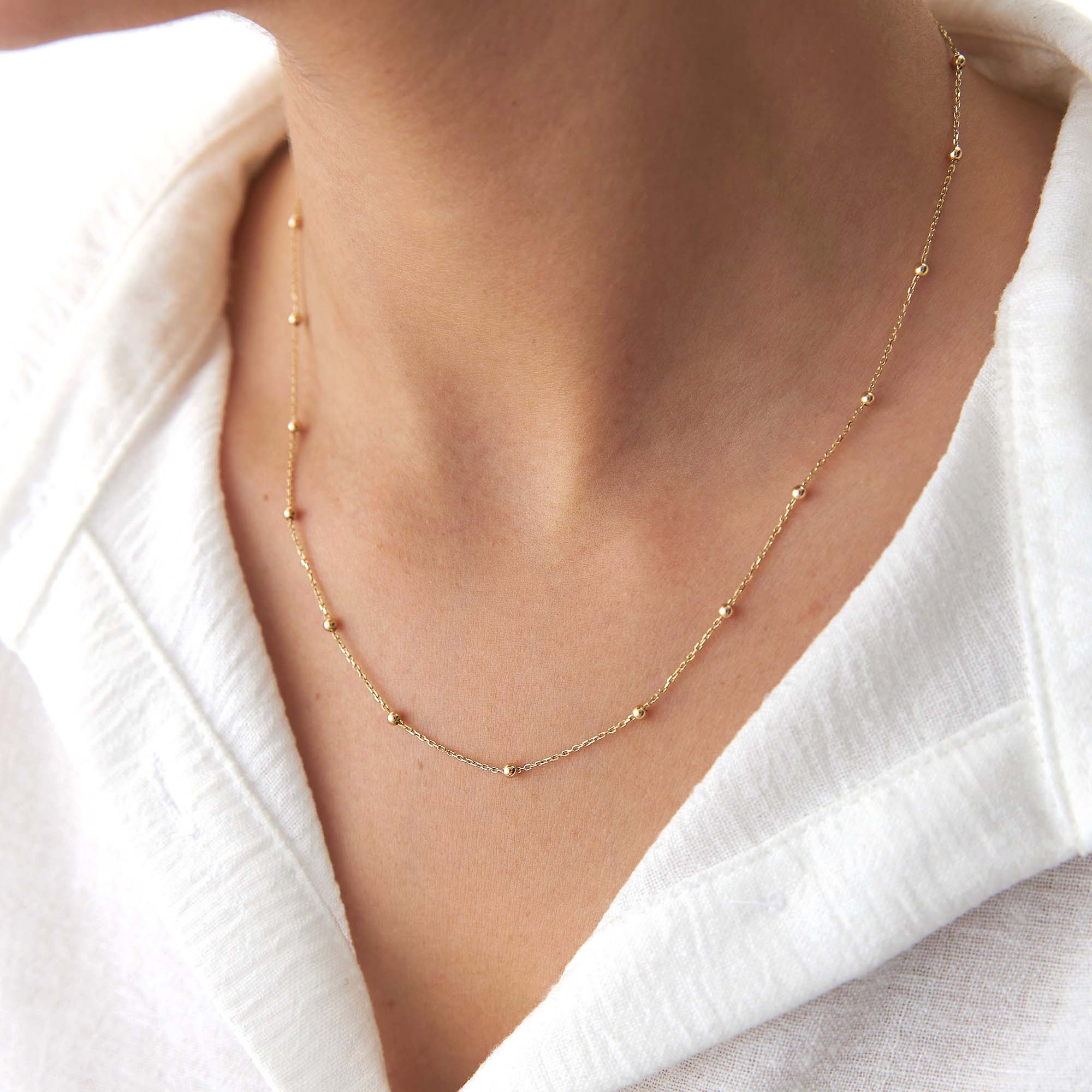 A 14k yellow gold satellite chain necklace on a model.