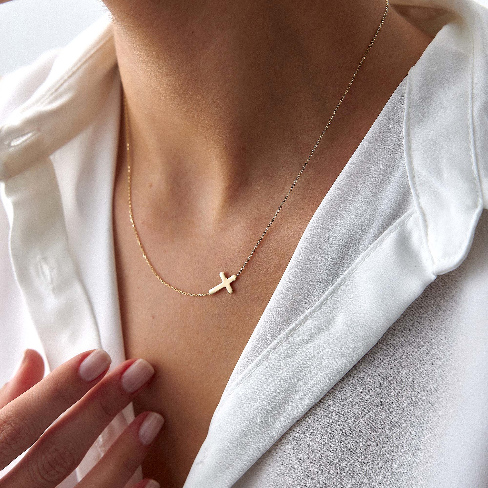 Gold necklace with a sideways cross pendant on a person wearing a white top.