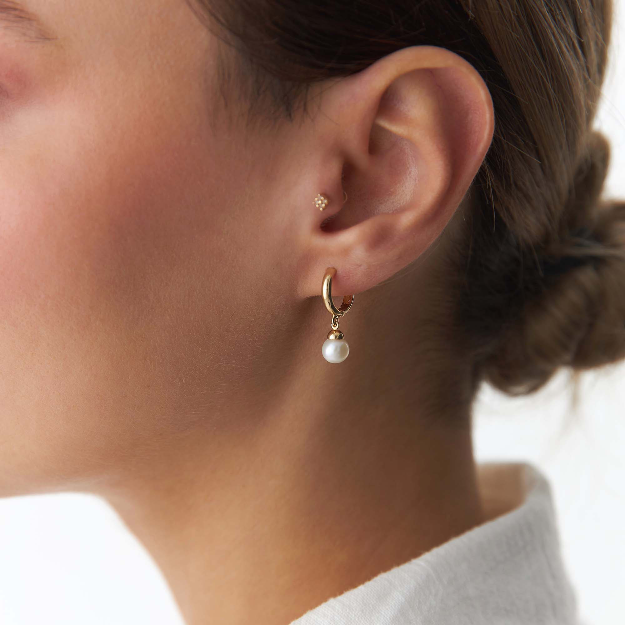 Gold hoop earring with a pearl drop worn by a person.