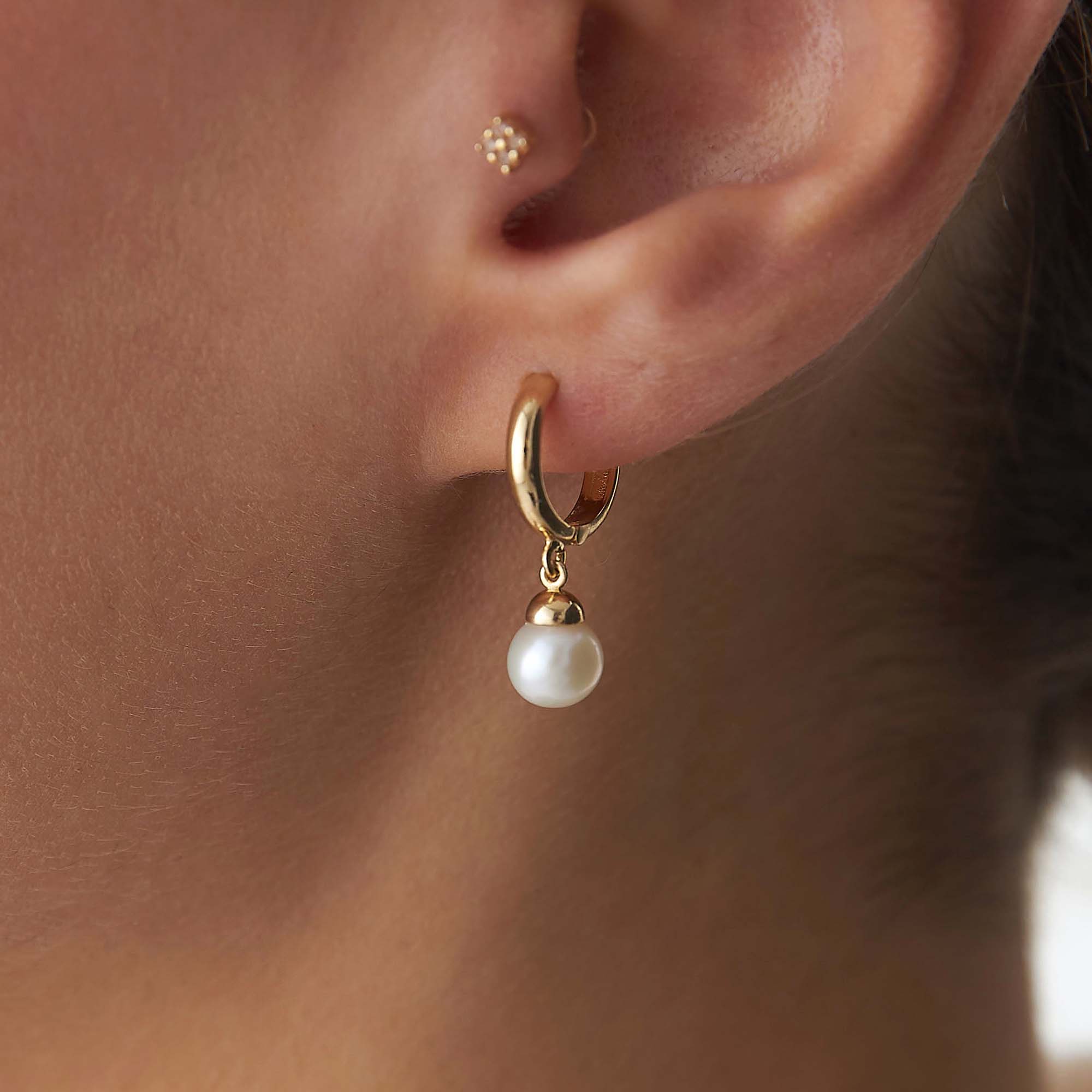 Gold hoop earring with a pearl drop worn by a person.