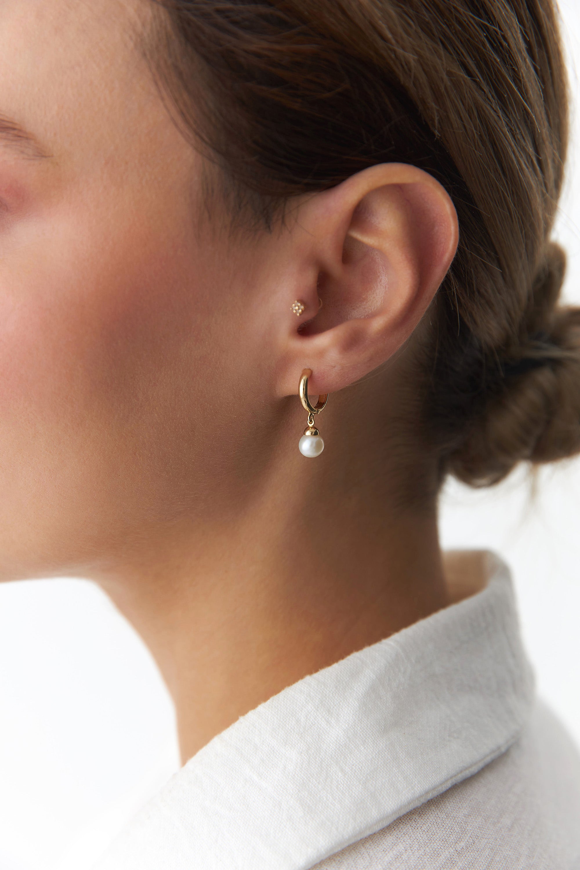 Gold hoop earring with a pearl drop worn by a person.