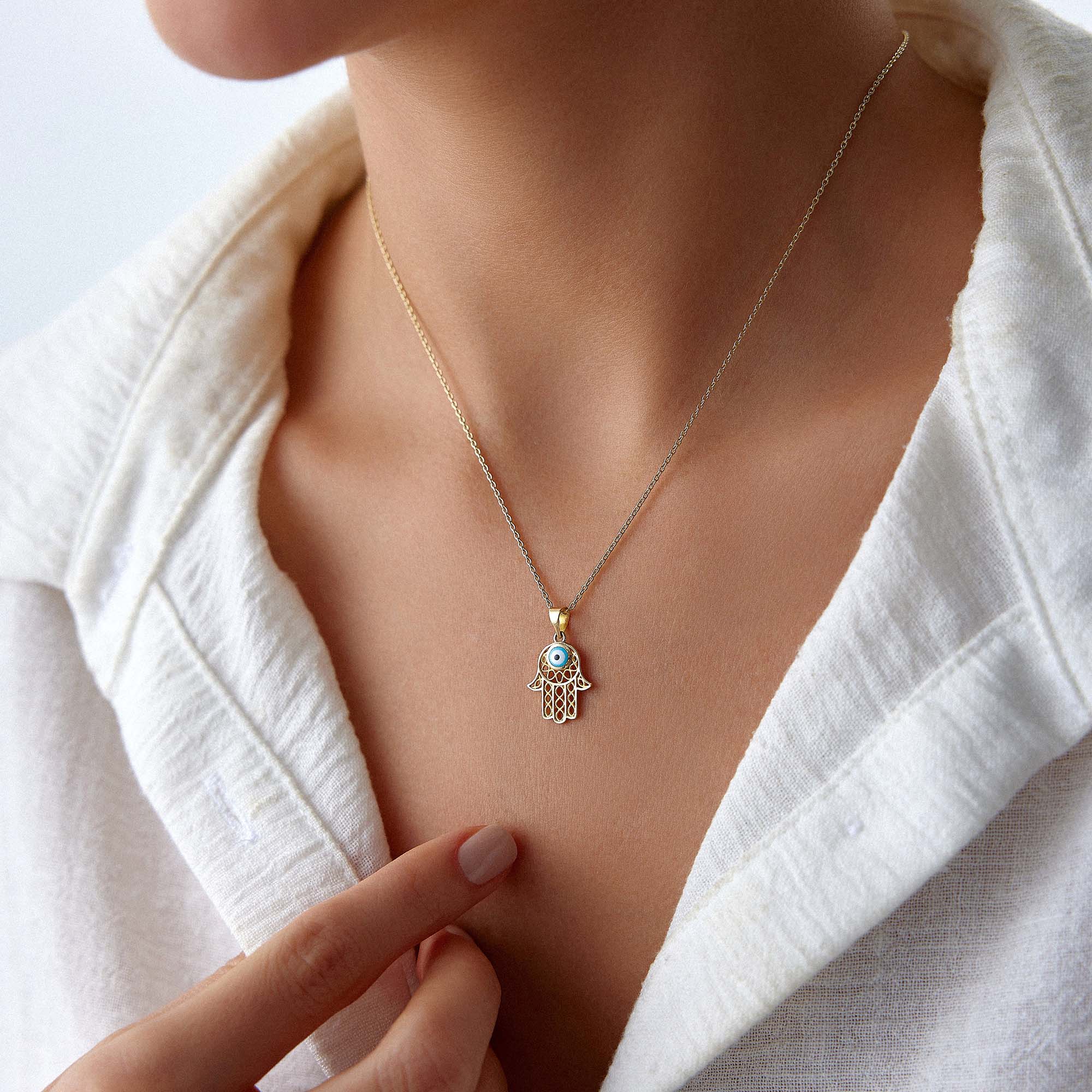 A model wearing a traditional small hamsa pendant with a blue evil eye center on a gold chain.