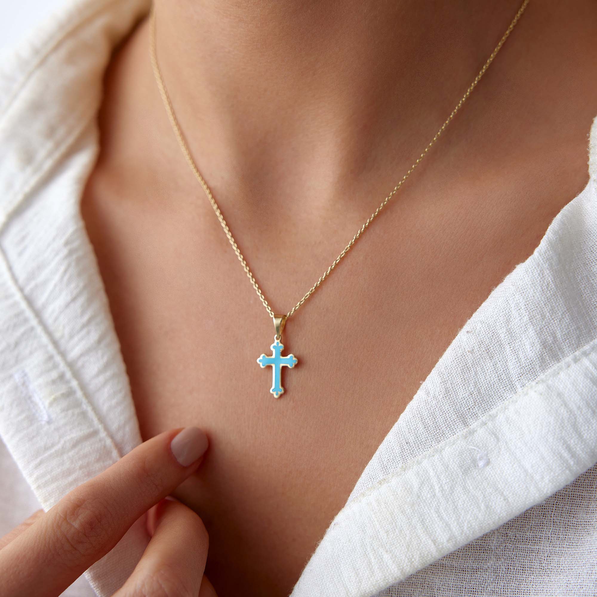 A model wearing a small ocean blue cross pendant on a thin gold chain