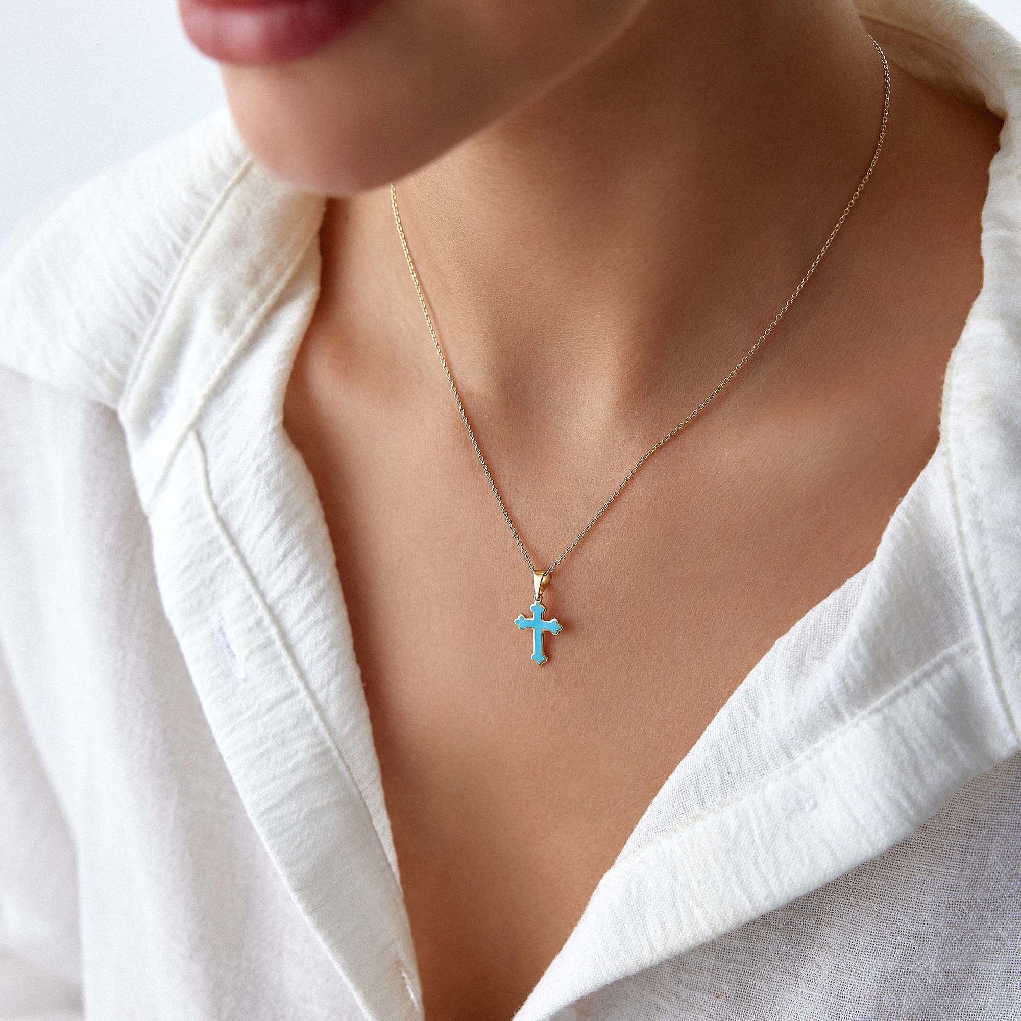 A model wearing a small ocean blue cross pendant on a thin gold chain