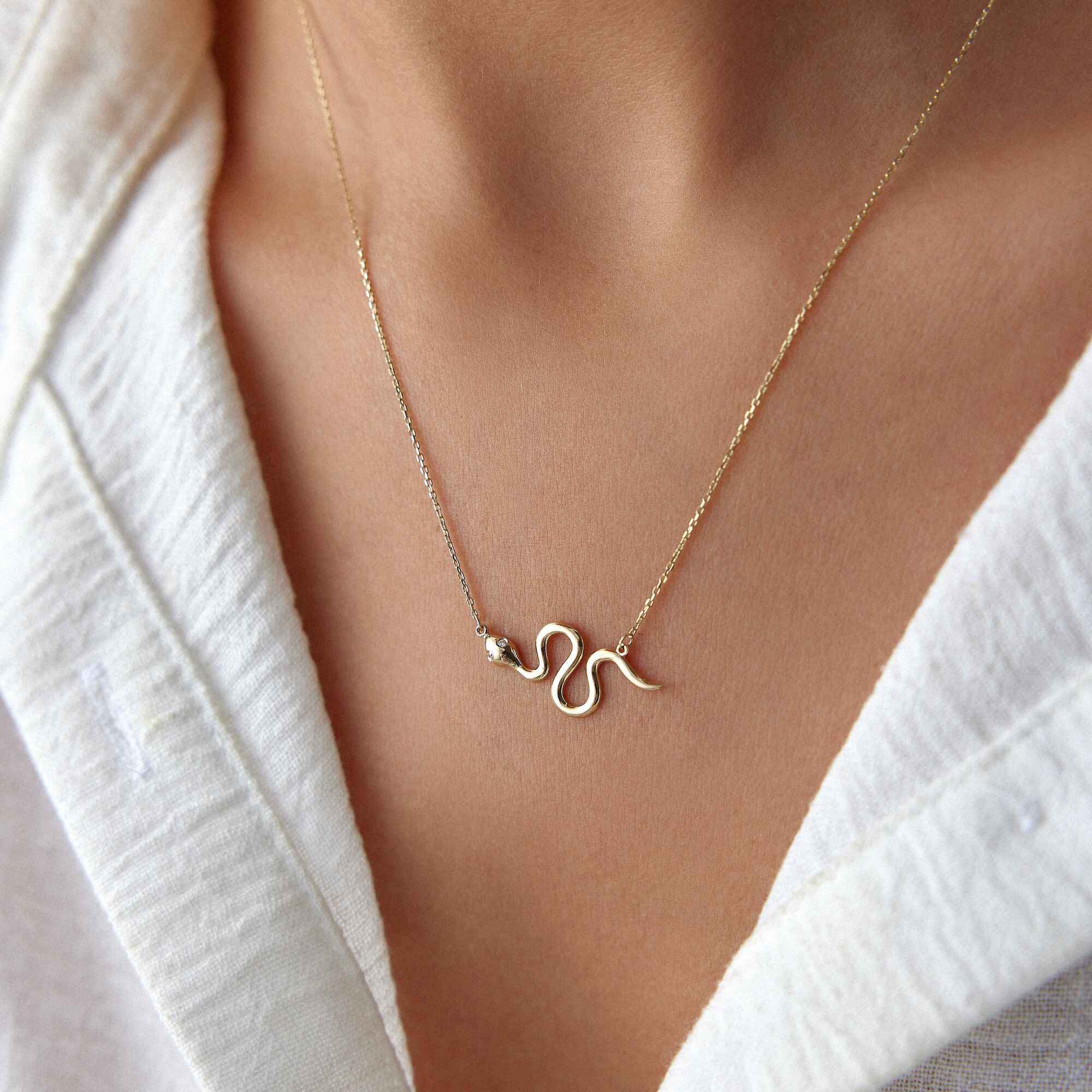 Gold snake necklace on a person wearing a white top