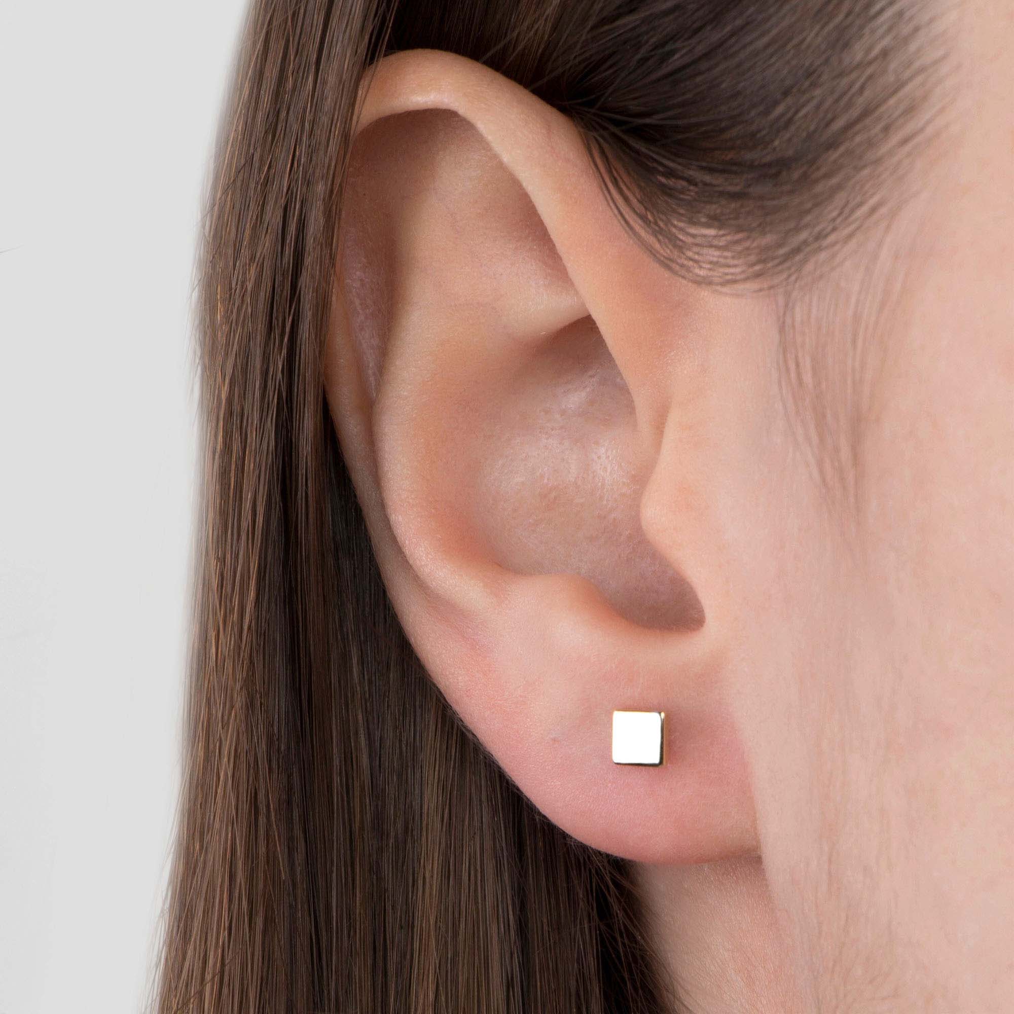 Close-up of an ear wearing a square stud earring against a neutral background