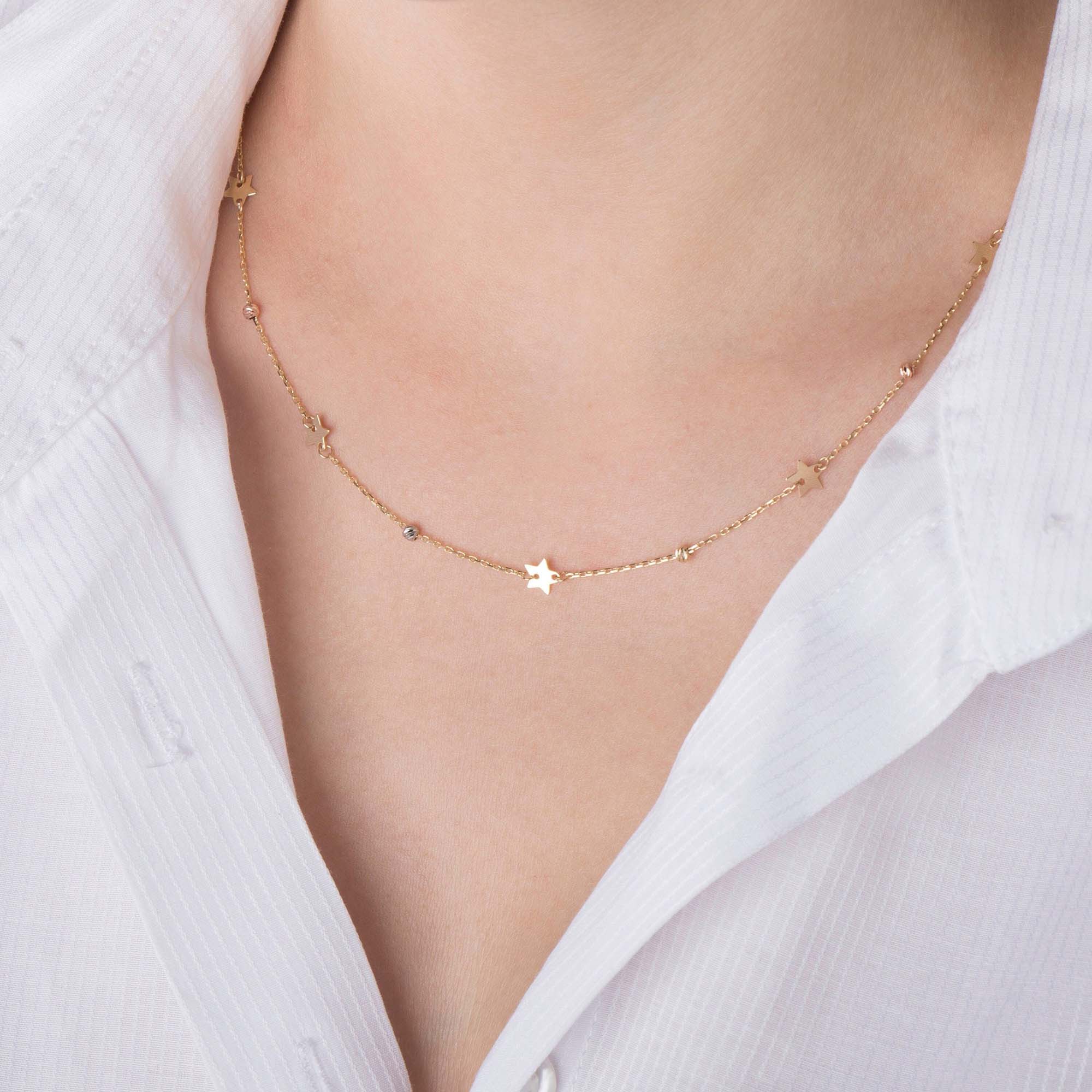 Gold star chain necklace on a person wearing a white top