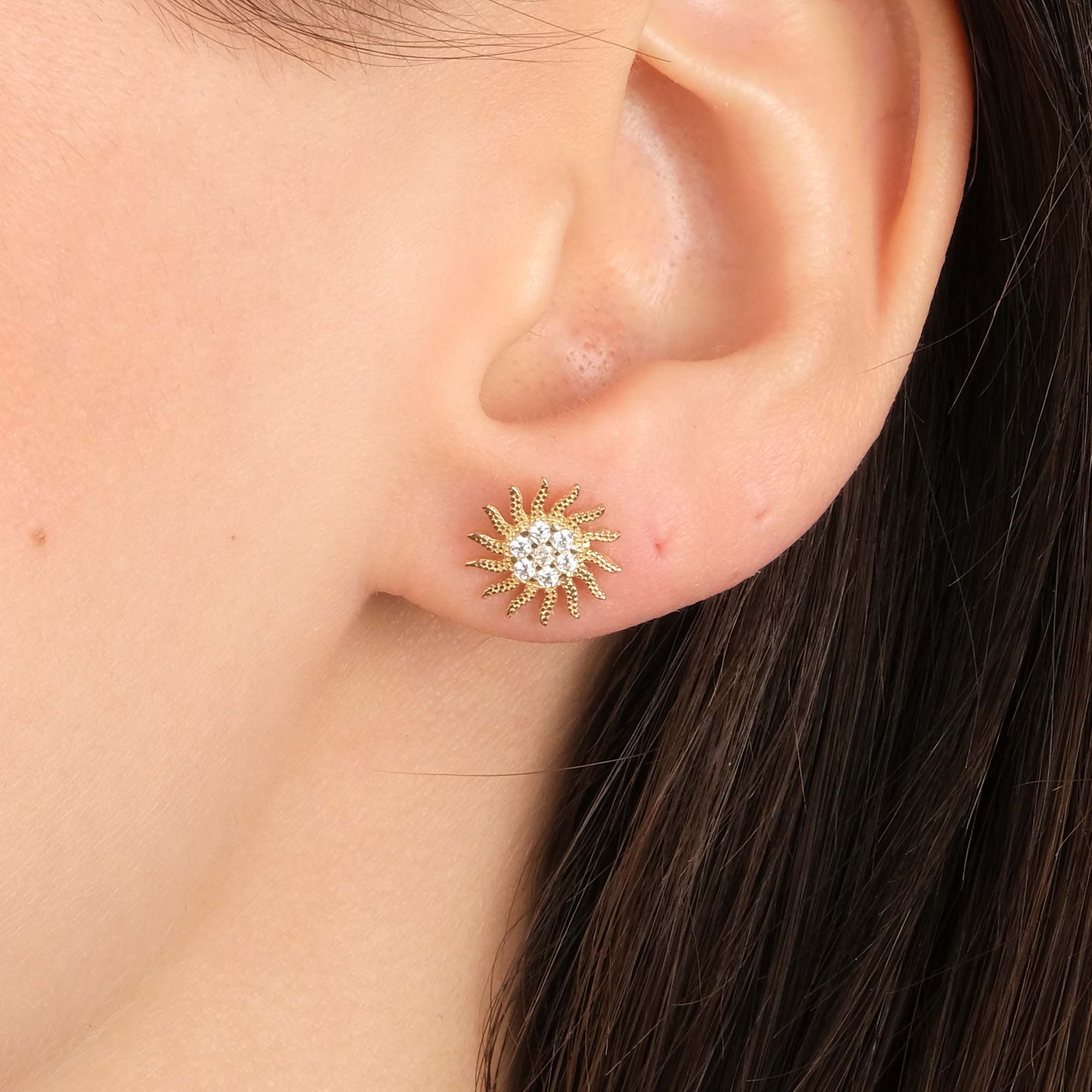 Close-up of an ear wearing a gold sun shaped earring.