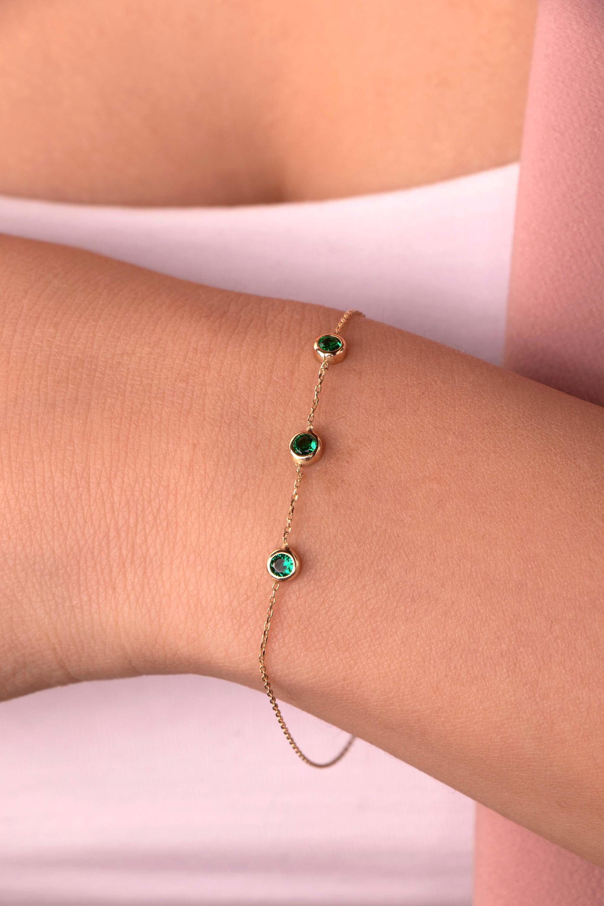 A created emerald bracelet in 14K yellow gold with a chain link and three bezel-set emeralds on the bracelet.