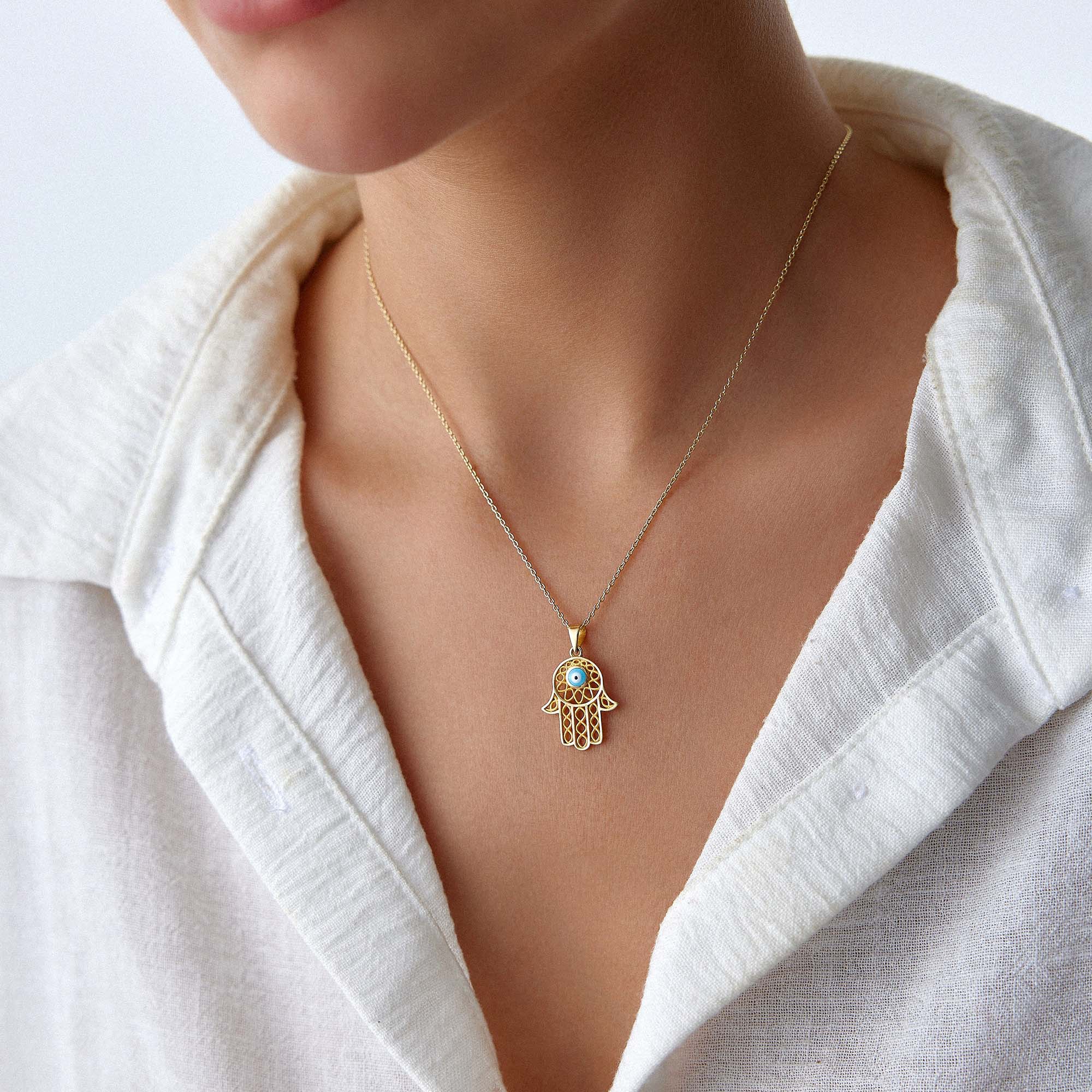 A model wearing a traditional large hamsa pendant with a blue evil eye center on a gold chain.