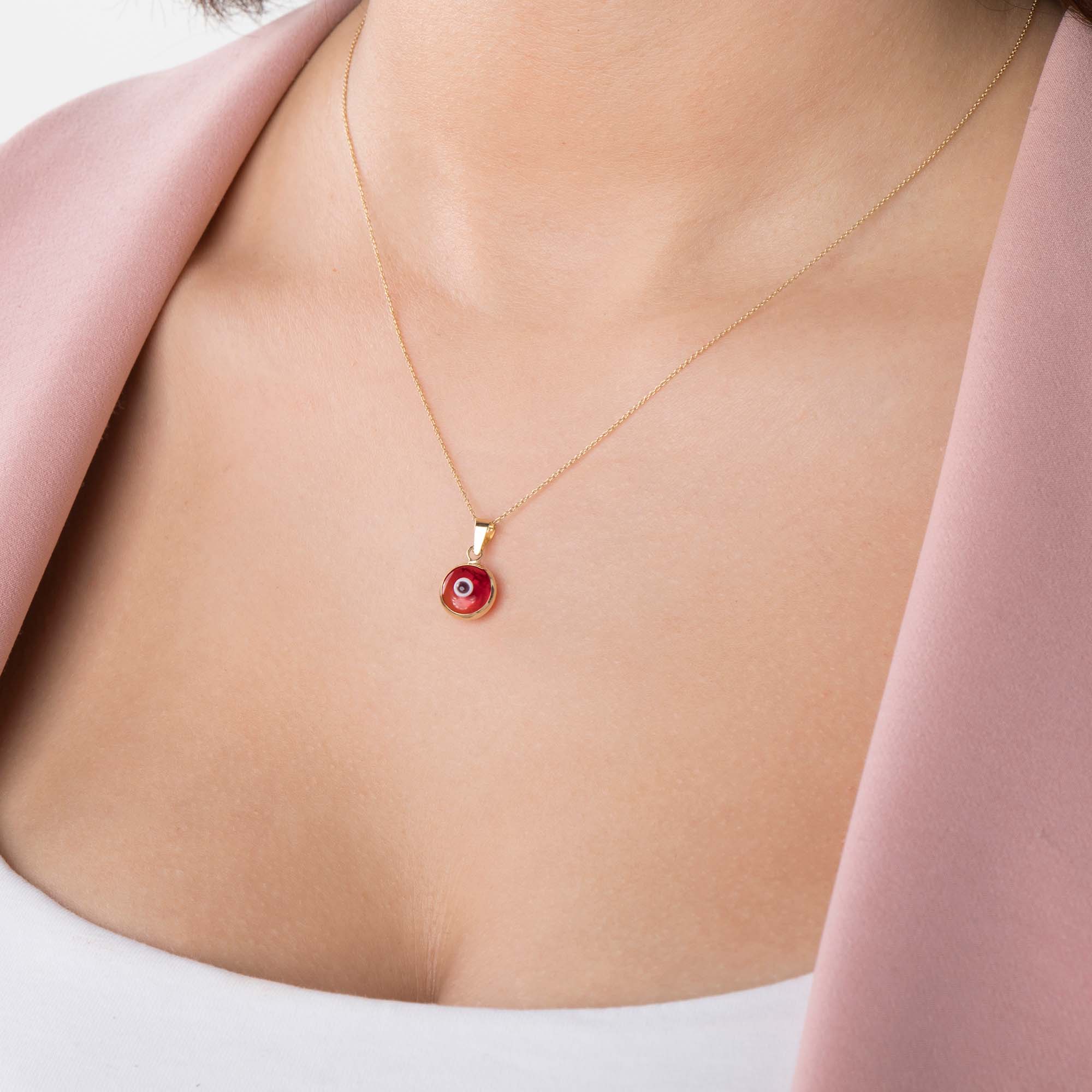 A model wearing a 14k yellow gold translucent red evil eye pendant on a chain