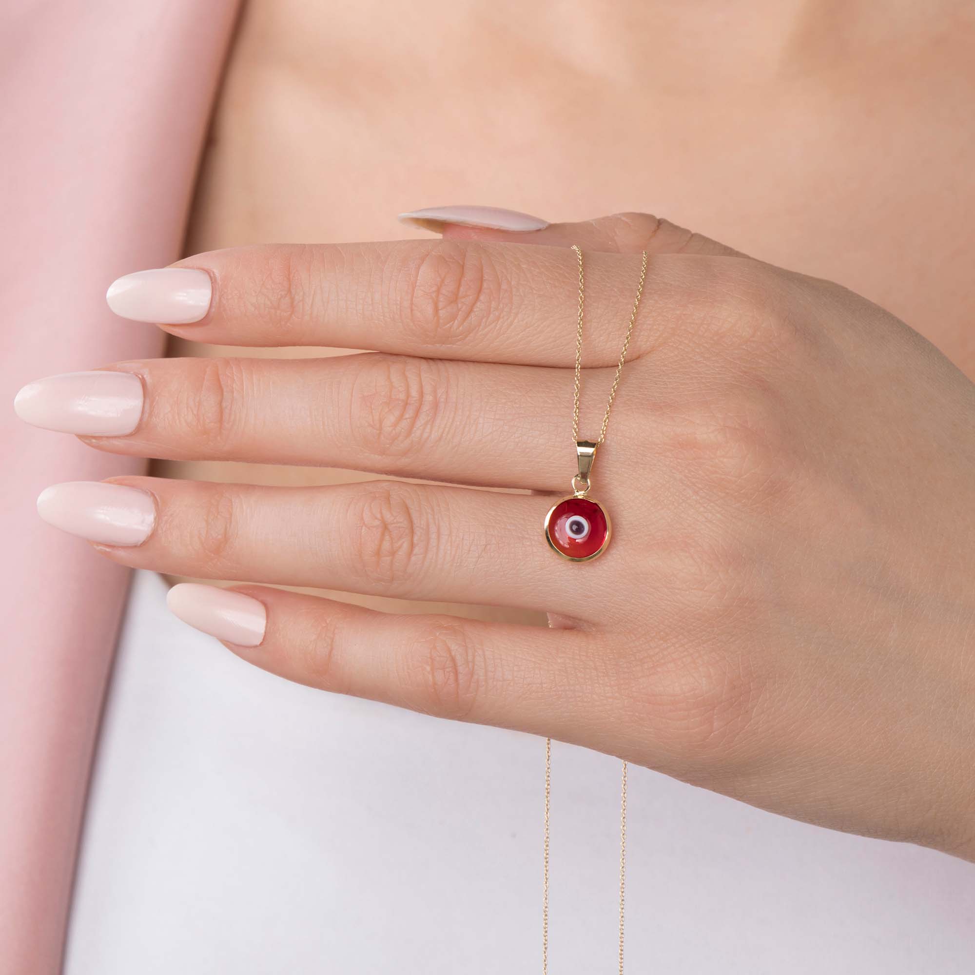 A model holding a 14k yellow gold translucent red evil eye pendant on a chain