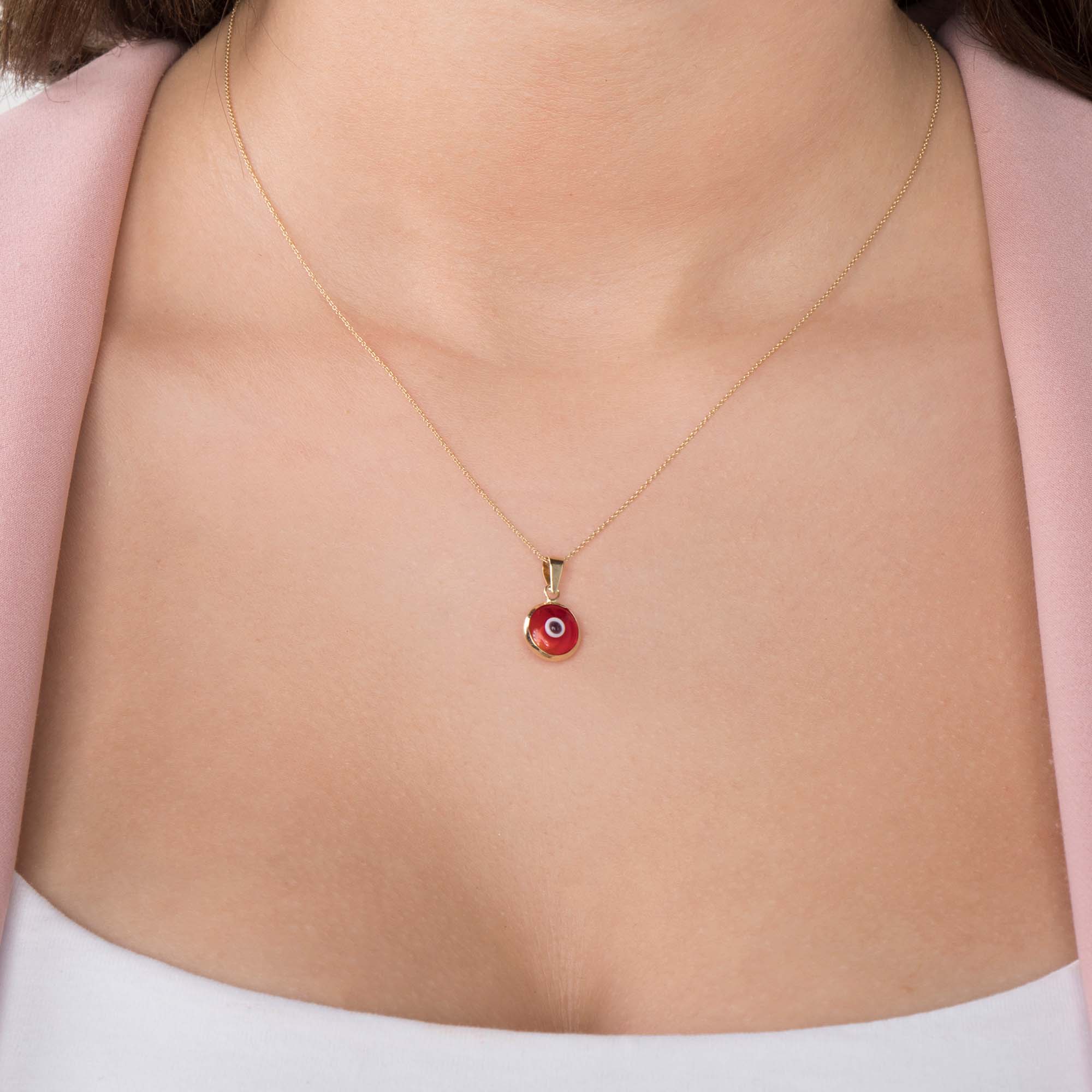 A model wearing a 14k yellow gold translucent red evil eye pendant on a chain