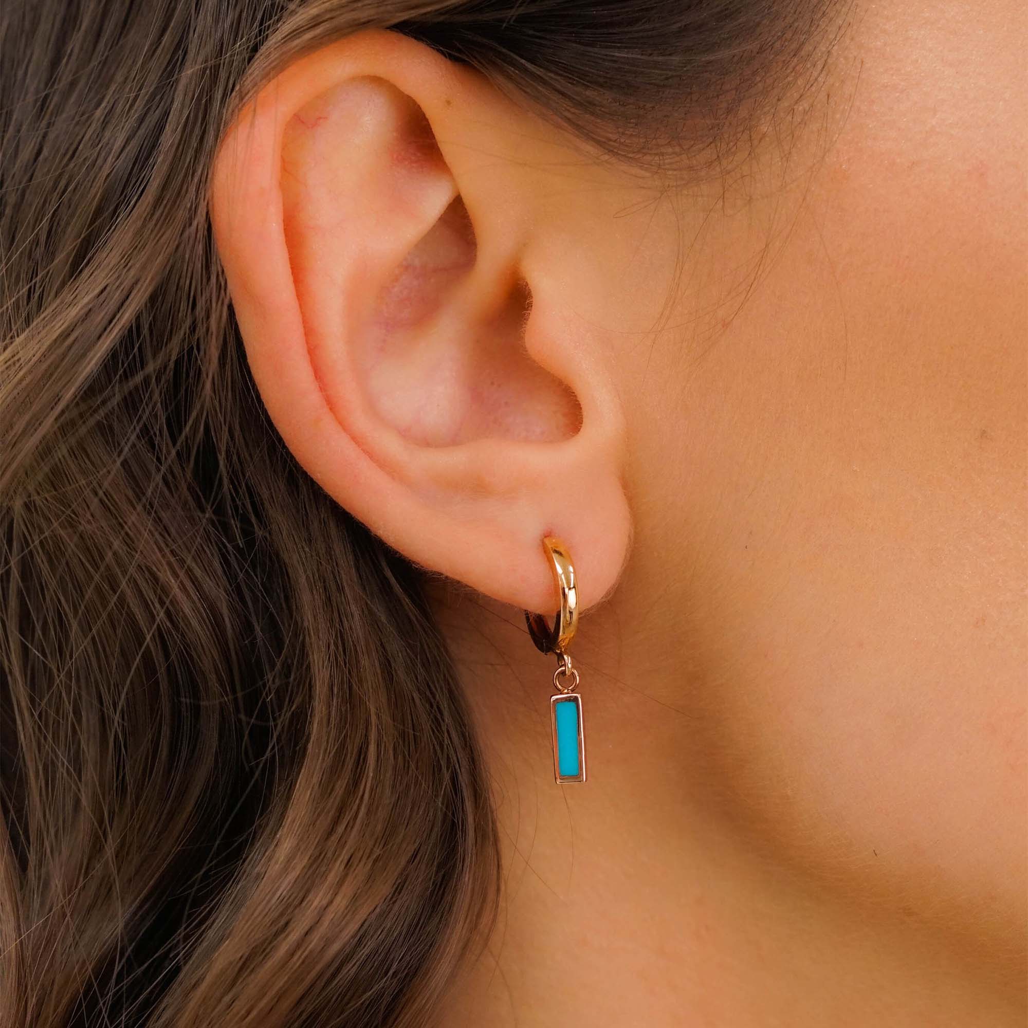 Close-up of an ear wearing a gold hoop earring with a turquoise bar charm.