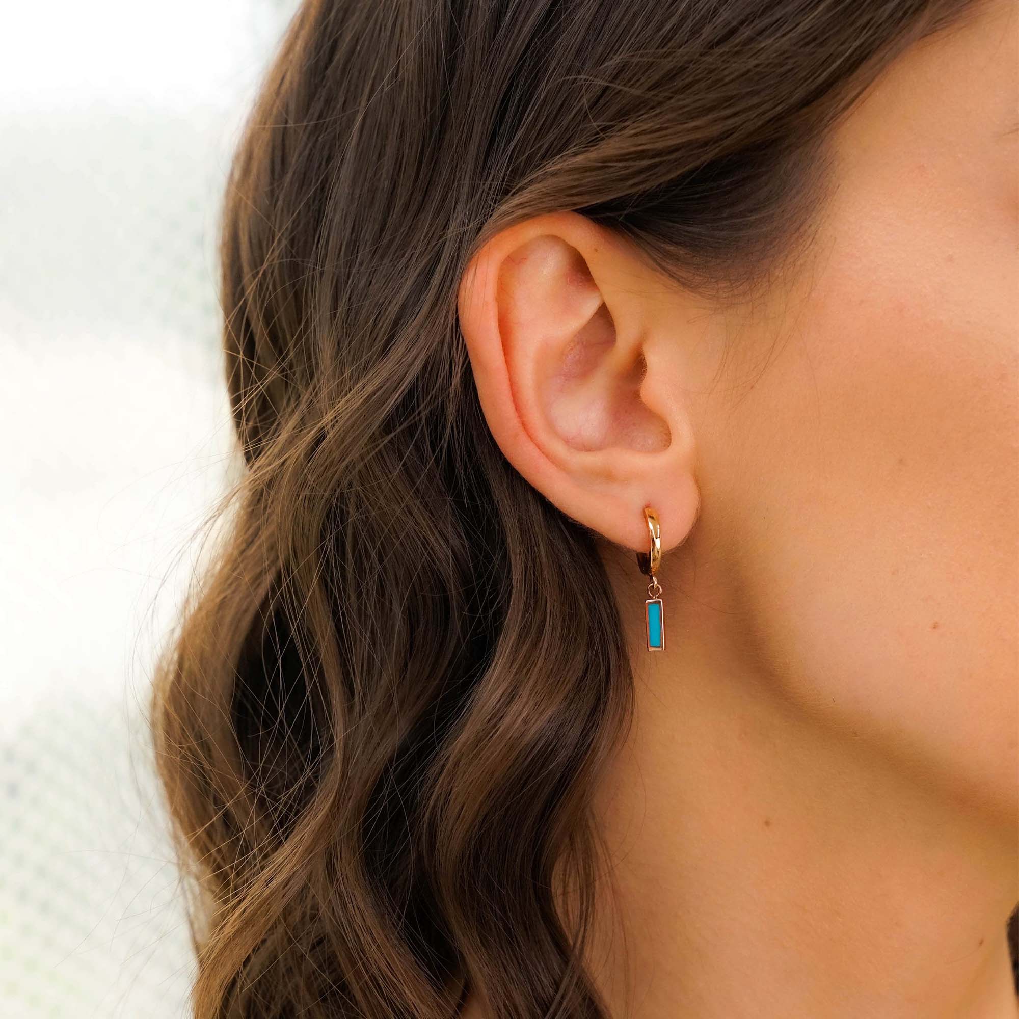 Close-up of an ear wearing a gold hoop earring with a turquoise bar charm.