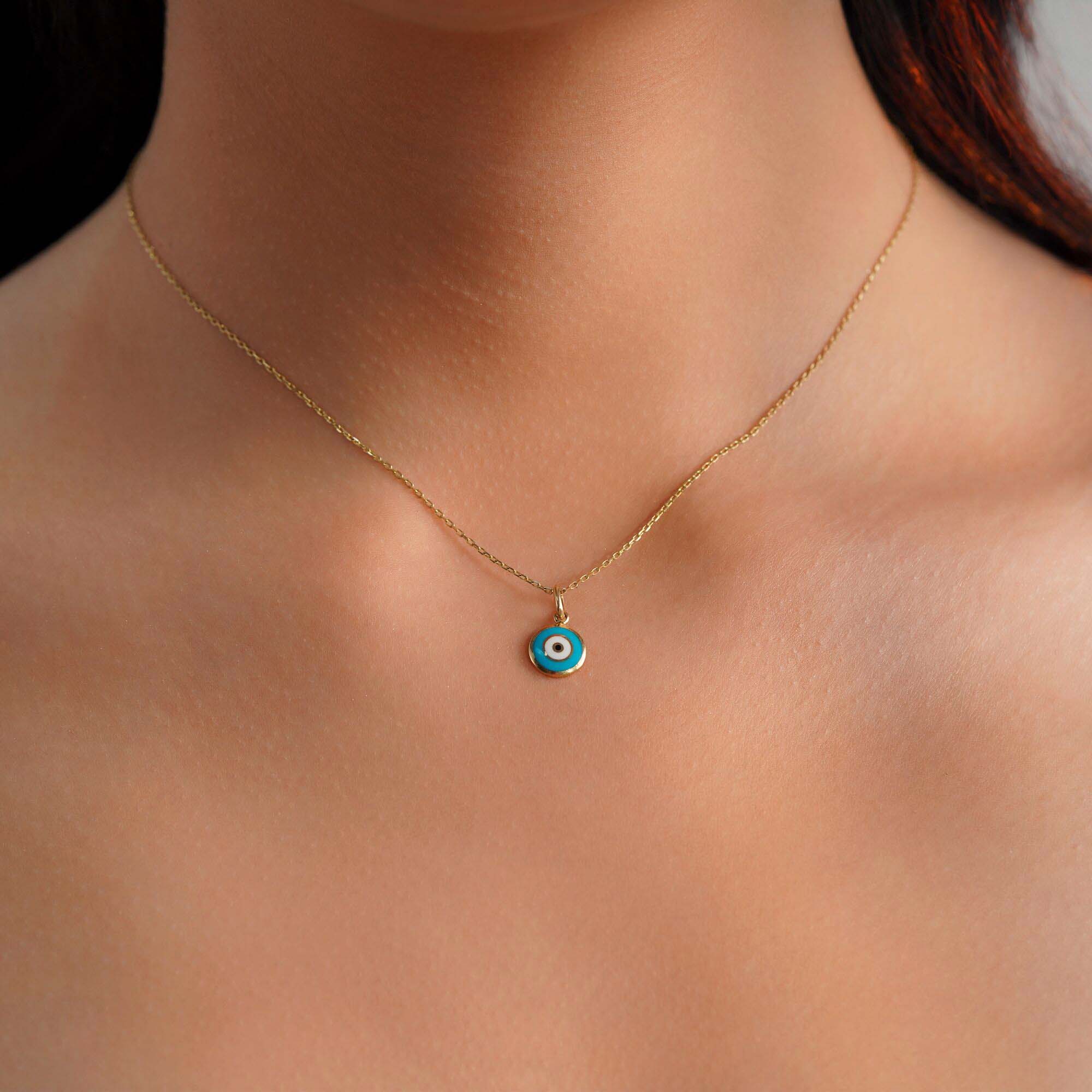 A model wearing a turquoise blue evil eye pendant on a gold chain.