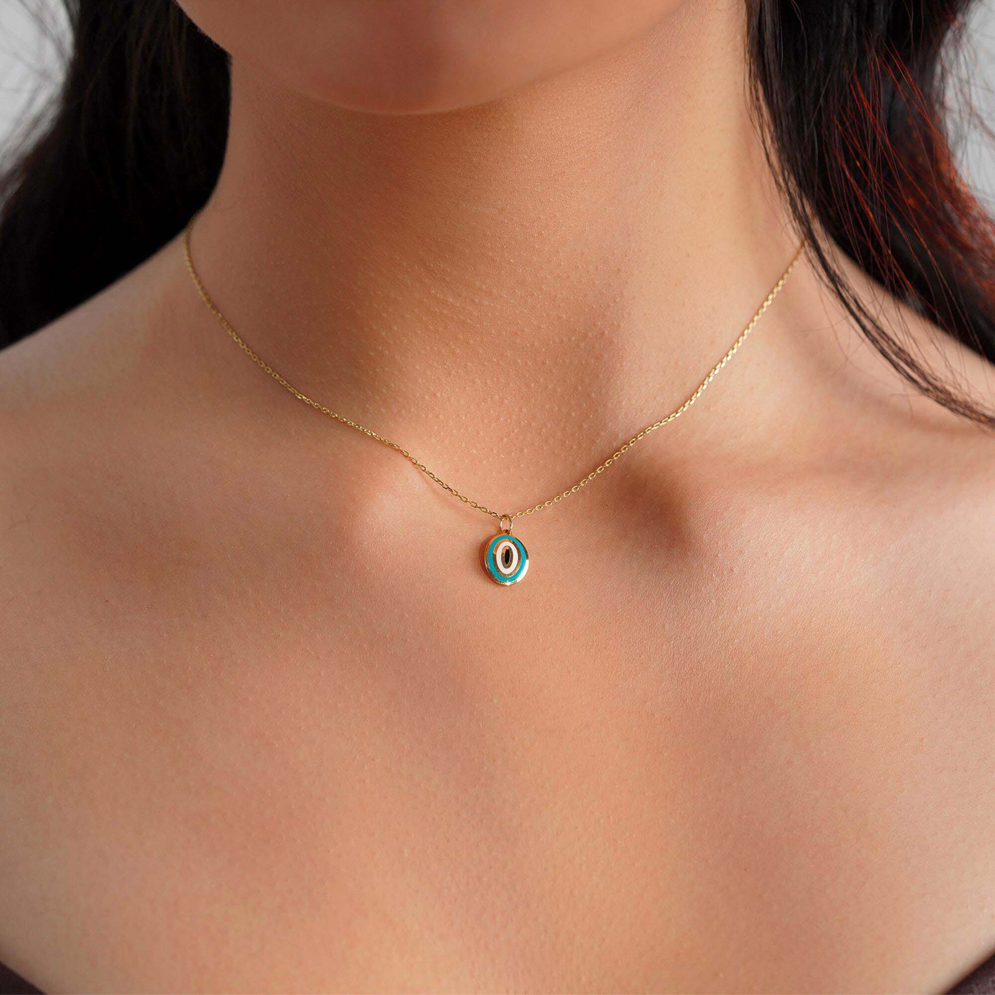 A model wearing an oval shaped turquoise evil eye pendant on a thin gold chain. 