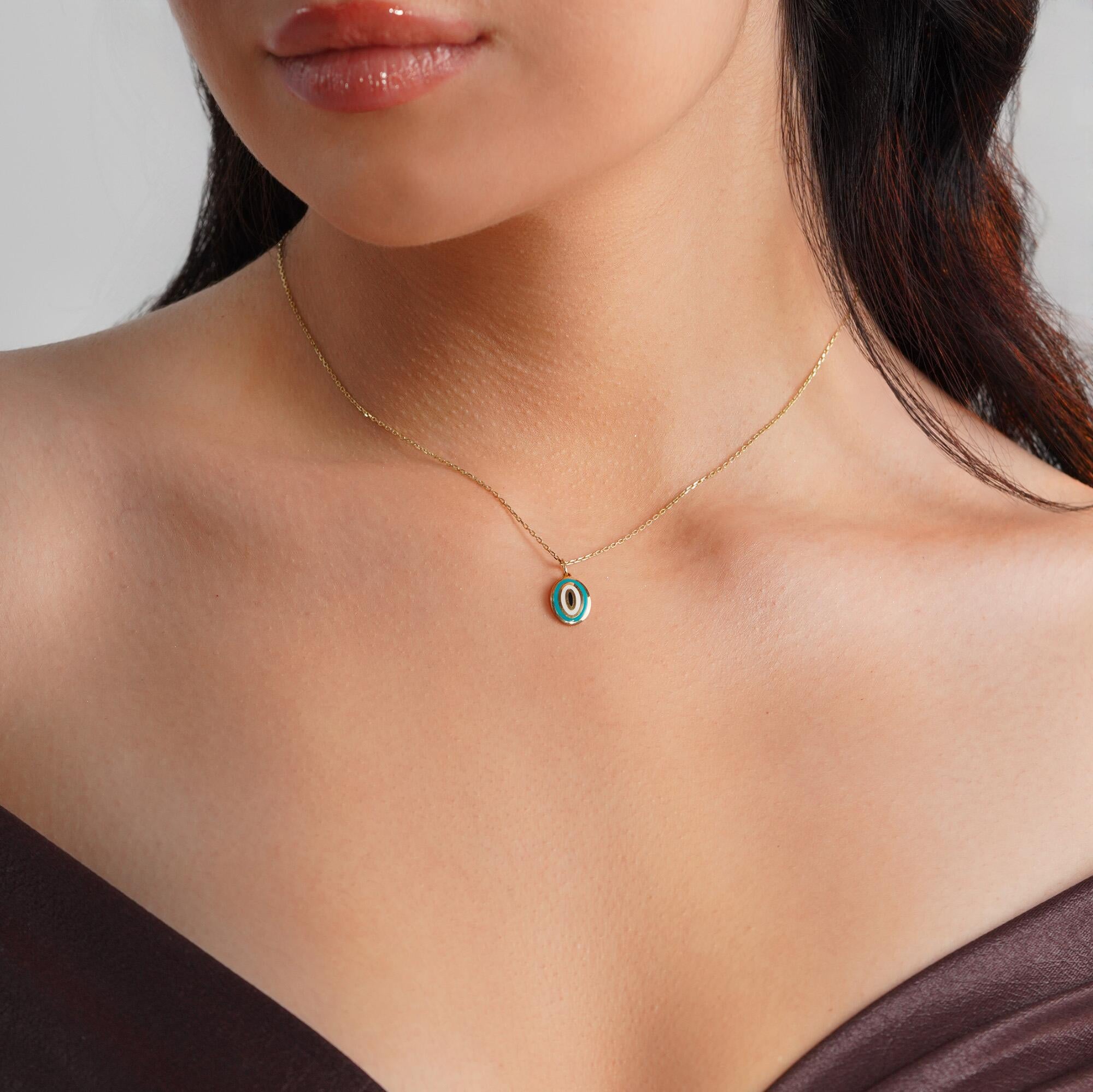 A model wearing an oval shaped turquoise evil eye pendant on a thin gold chain. 