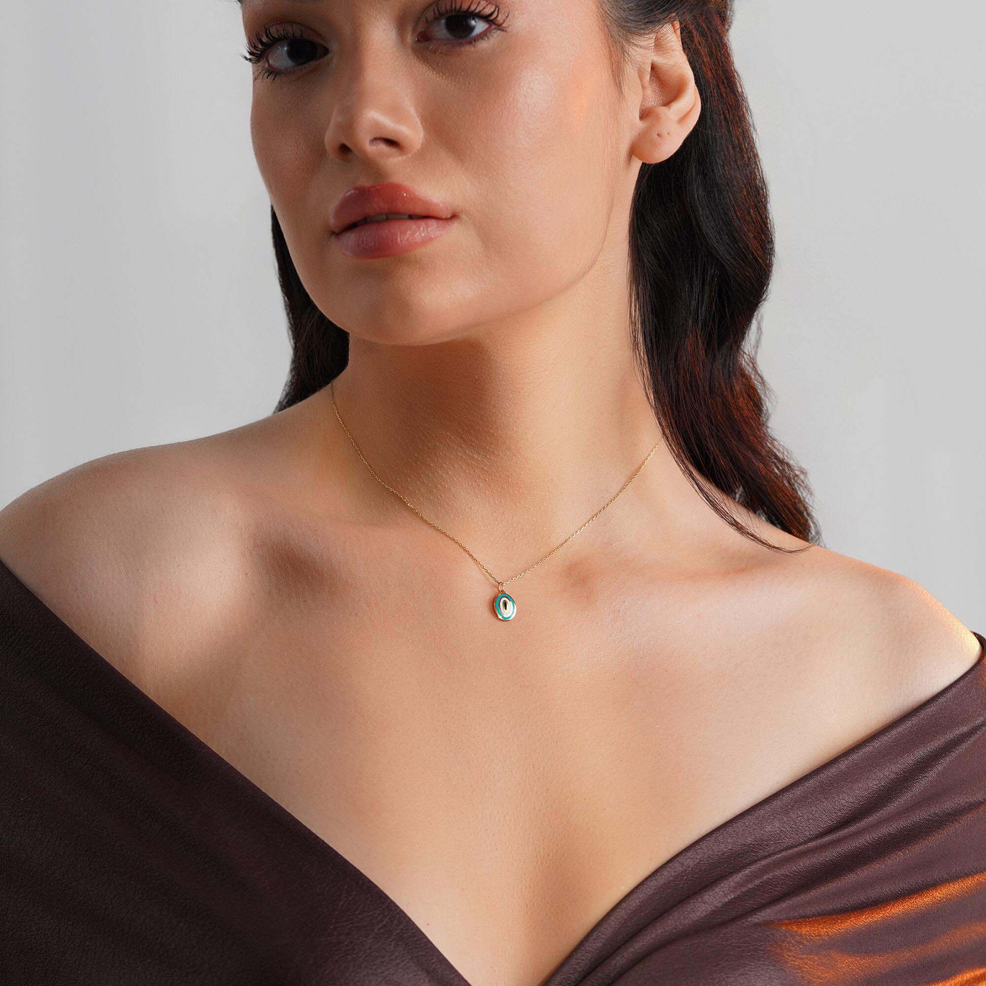 A model wearing an oval shaped turquoise evil eye pendant on a thin gold chain. 