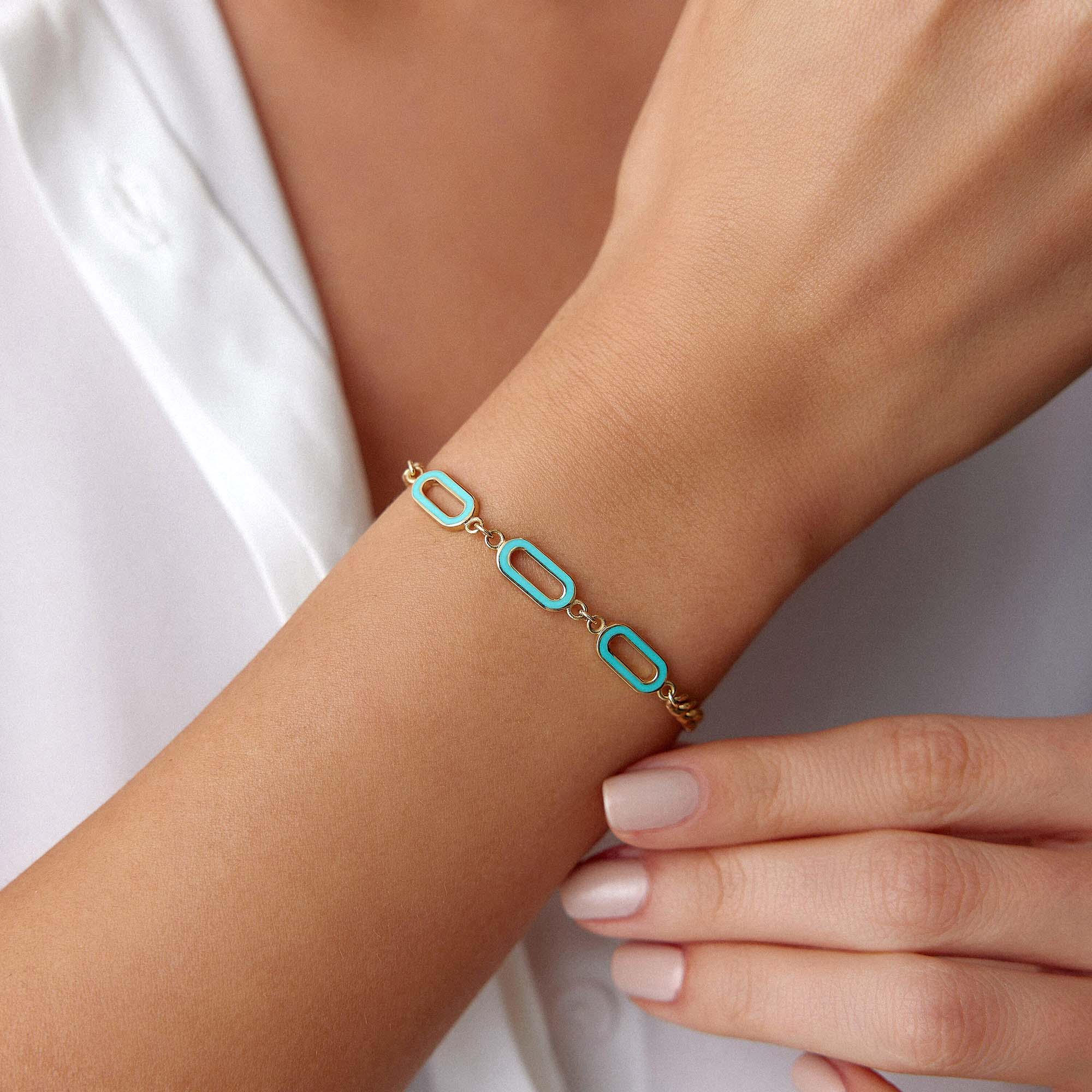 A 14K gold solid oval link chain bracelet with turquoise enamel accents on the central links, displayed on a wrist.