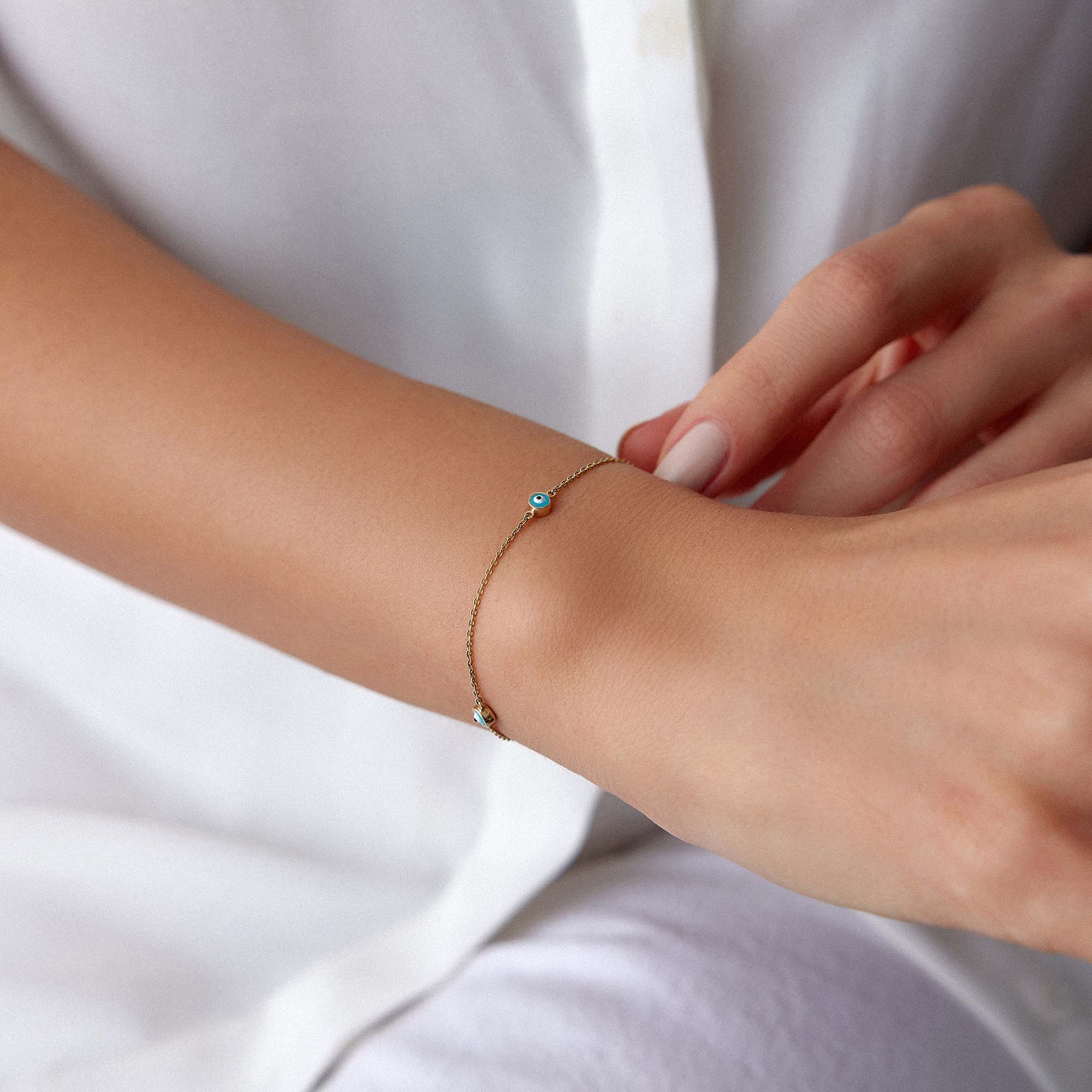 Person wearing a delicate bracelet with small evil eyes on a plain background