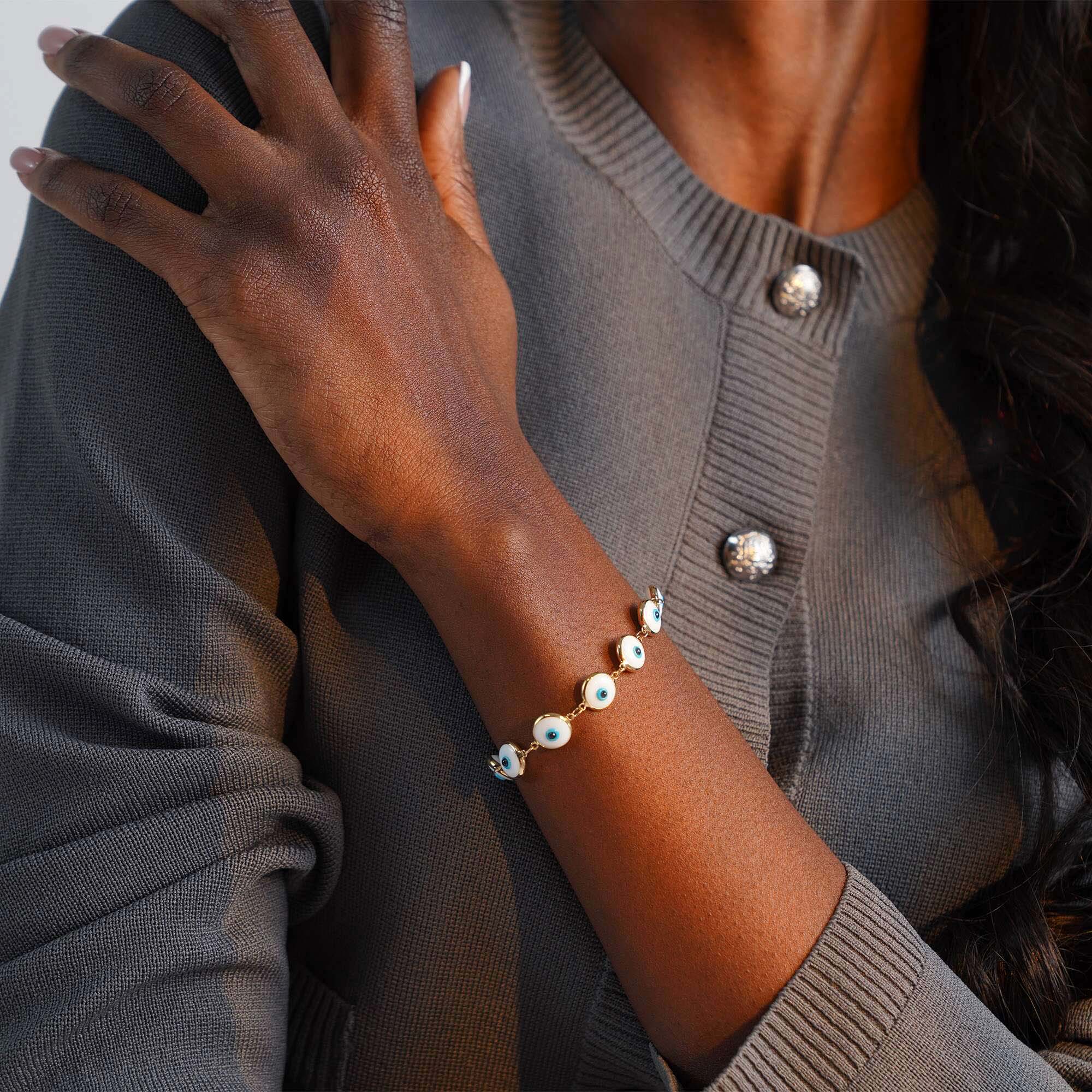 Person wearing a bracelet with white evil eye charms on a plain background