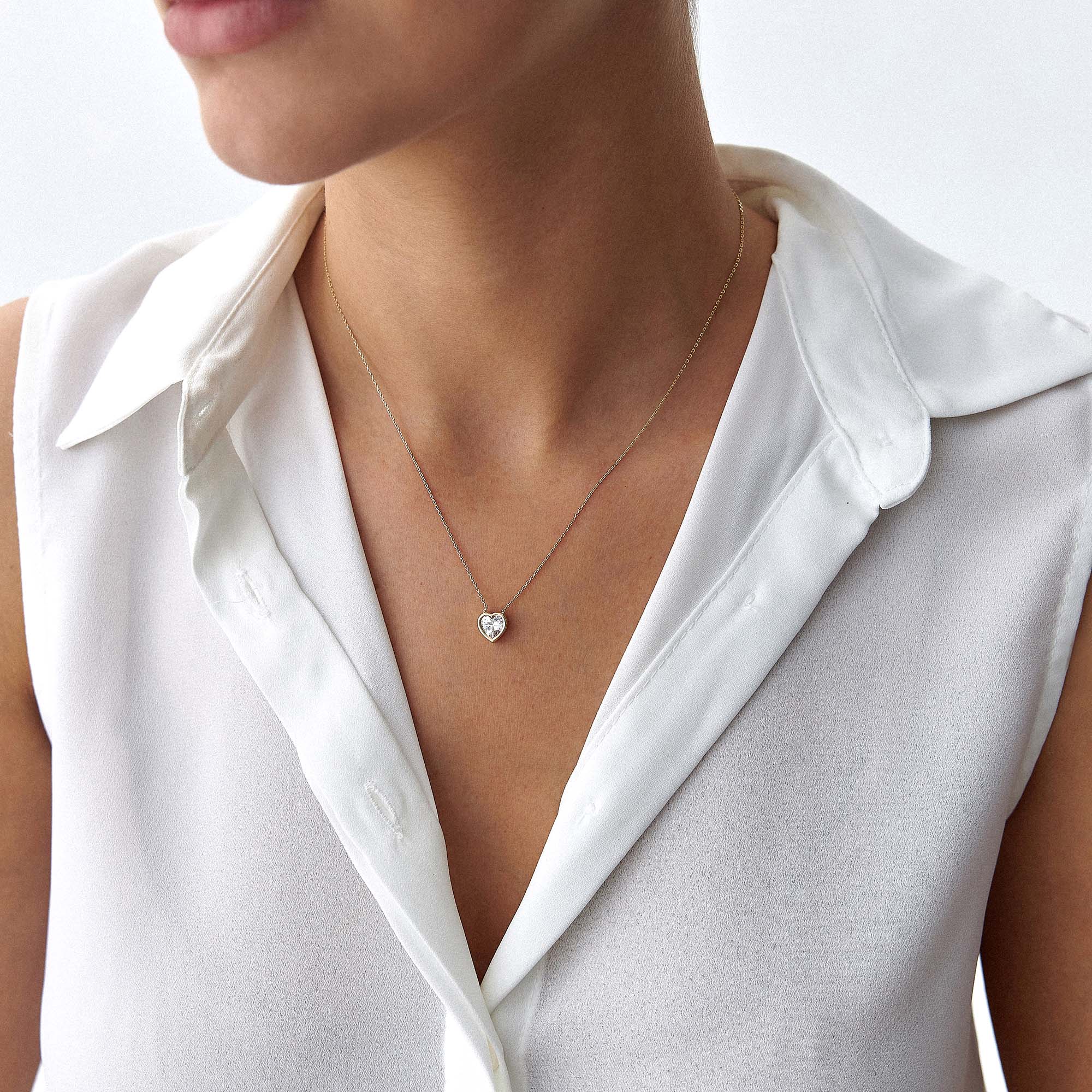 Person wearing a delicate necklace with a heart pendant on a plain background