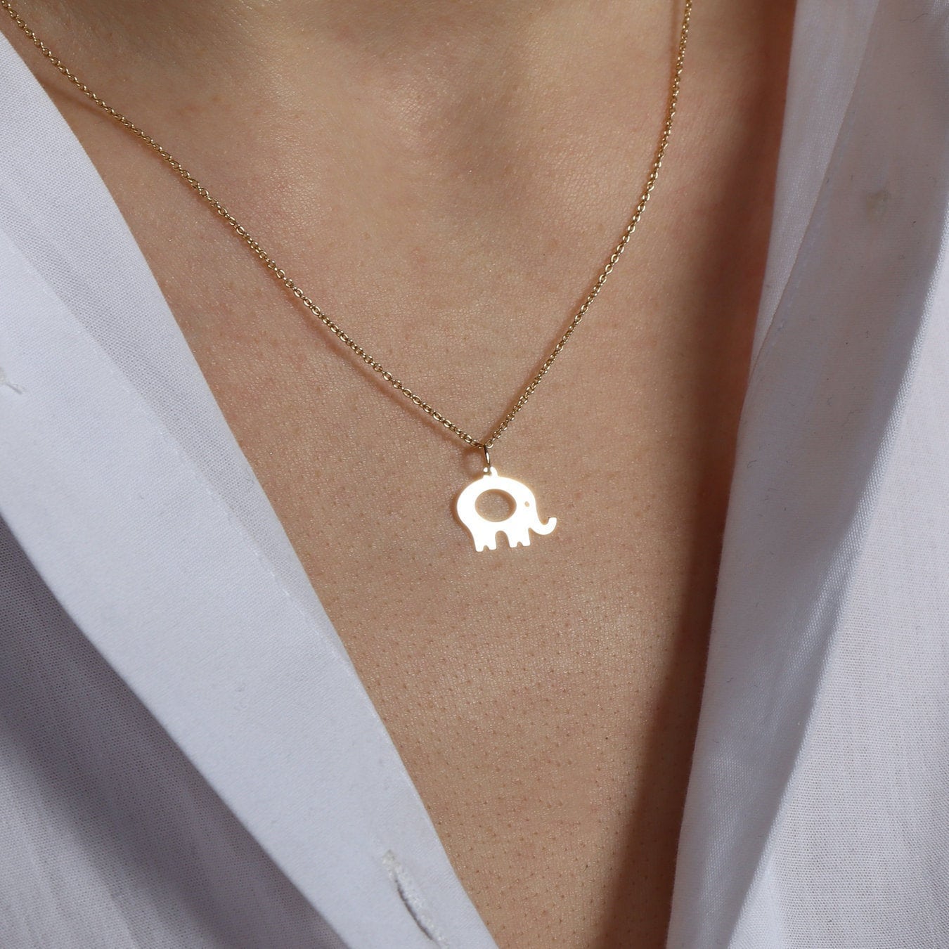 A 14k yellow gold minimal elephant necklace worn by a model.